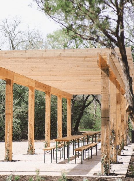 A wooden structure with benches under it. Trees in the background.