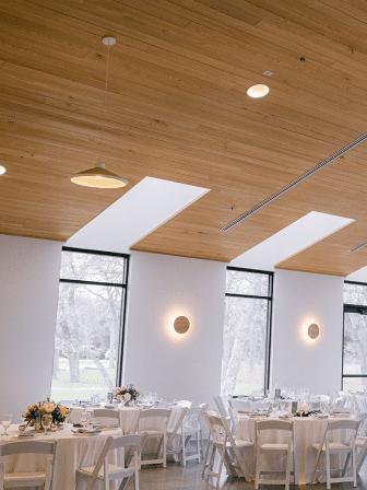 A large room with tables and chairs in it. There are lights on the ceiling above them.