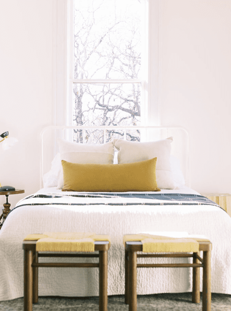 A bed with two stools in front of the window.