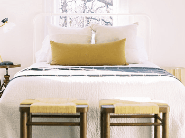 A bed with two stools in front of the window.