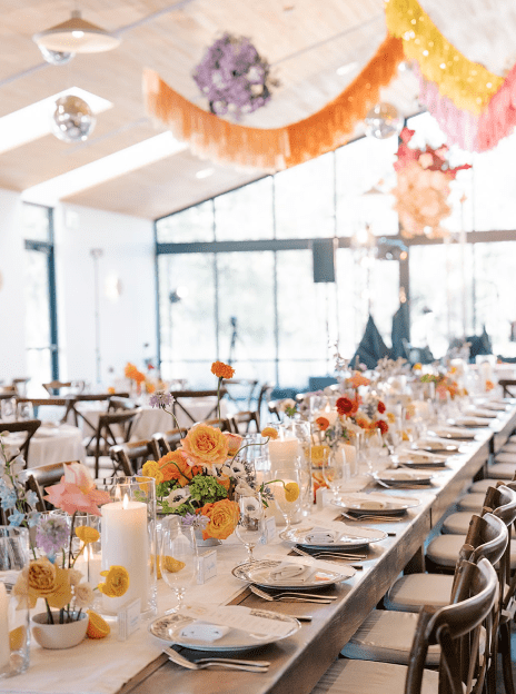 A long table with many glasses and flowers on it. The tables are set for an event.