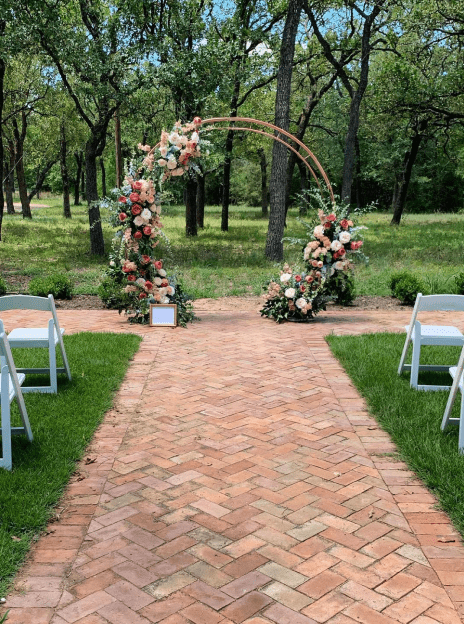 A wedding arch with flowers and chairs in the middle of an aisle.