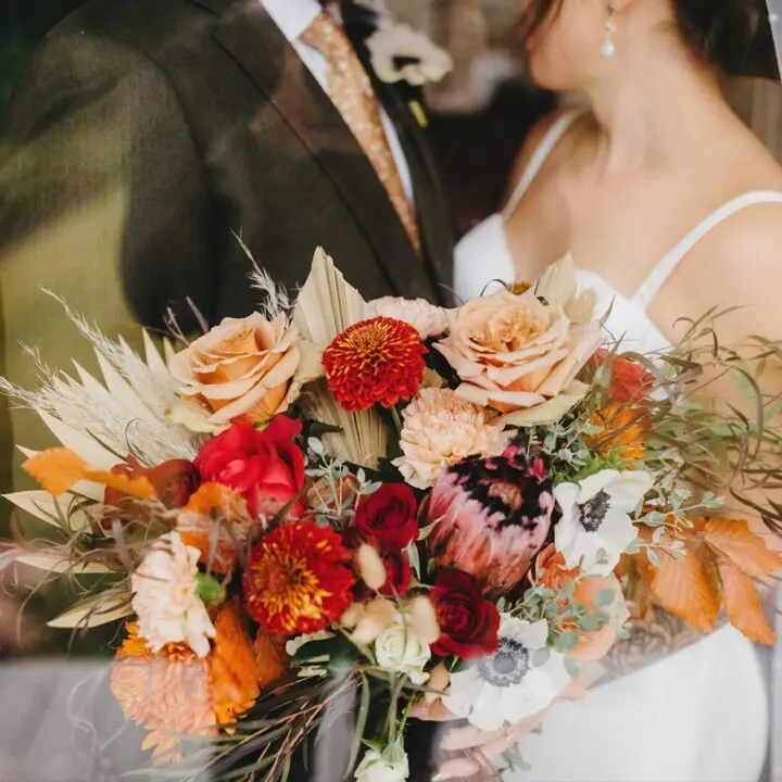 A bride and groom holding their bouquet of flowers. They are standing in front of each other.