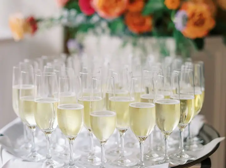 A table full of champagne glasses with flowers in the background.