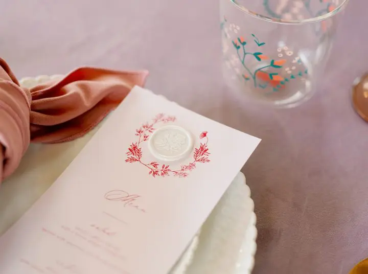 A close up of a menu on top of a plate. Next to a glass cup and napkin