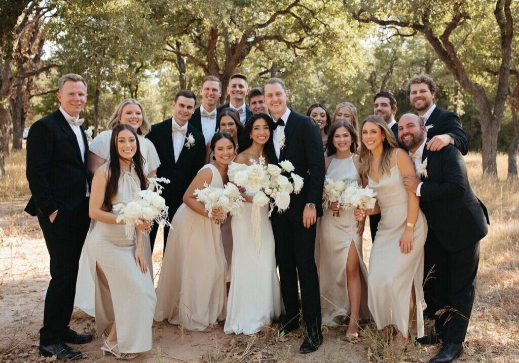 A group of people in formal wear posing for a picture. They are holding white flowers.